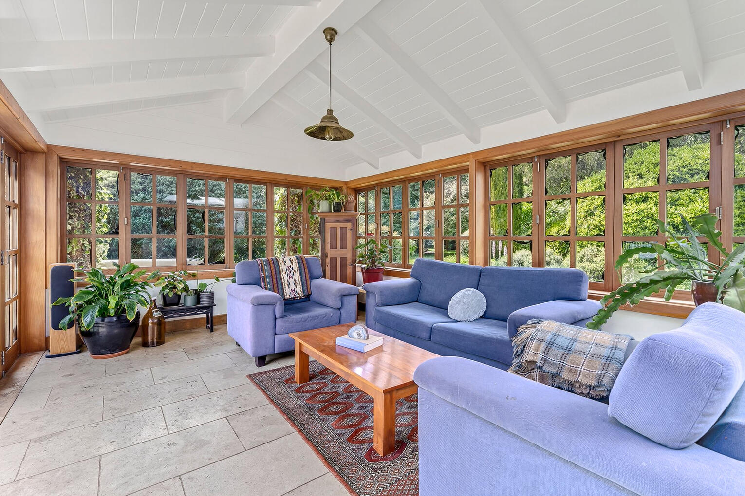 Decluttering · interior & exterior Styling · Property Staging Sunlit conservatory lounge with floor-to-ceiling windows, lush greenery views, and comfortable blue seating
