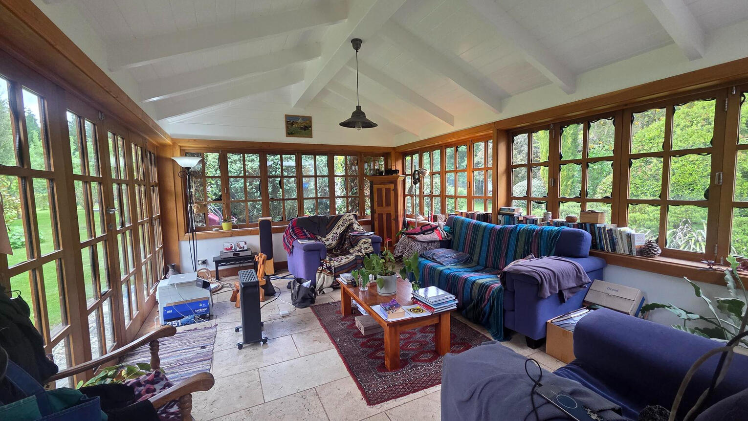 Decluttering · interior & exterior Styling · Property Staging Glass-enclosed sunroom with large windows overlooking trees, blue sofas, and a patterned rug